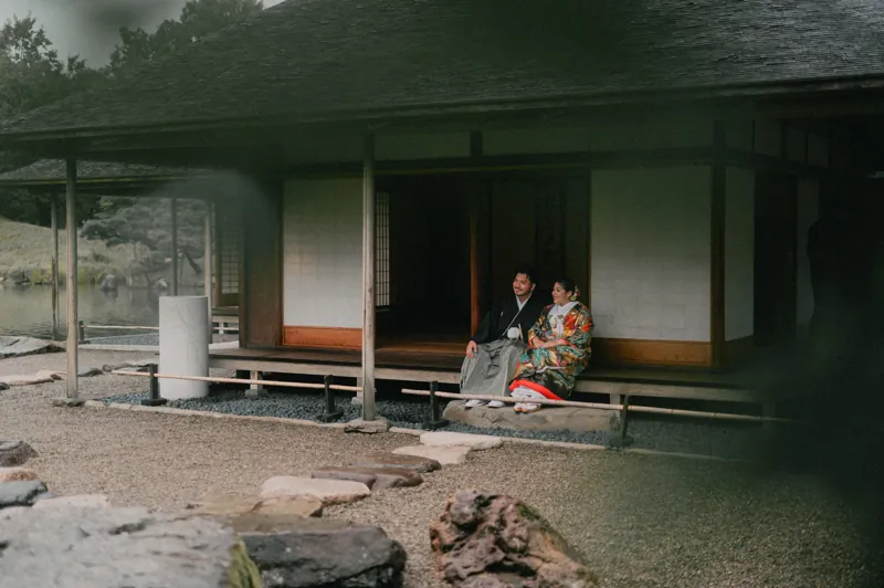 養浩館庭園の池に面した建物の縁側に、色打掛と紋付袴で並んで座るおふたり