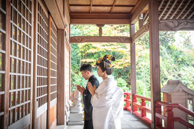神社の朱色の回廊で手を合わせるおふたり
